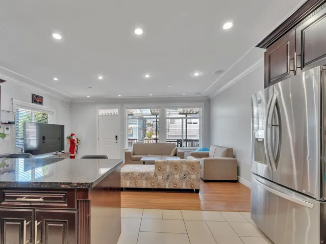 Open concept living space featuring a kitchen island with a dark countertop and wood-finish cabinetry, stainless steel refrigerator, recessed lighting, crown molding, and wood-finish flooring in the living area
