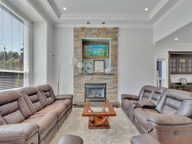 Living area featuring a stone-clad fireplace with an integrated firebox, high ceilings with crown molding and recessed lighting, and large windows with horizontal blinds