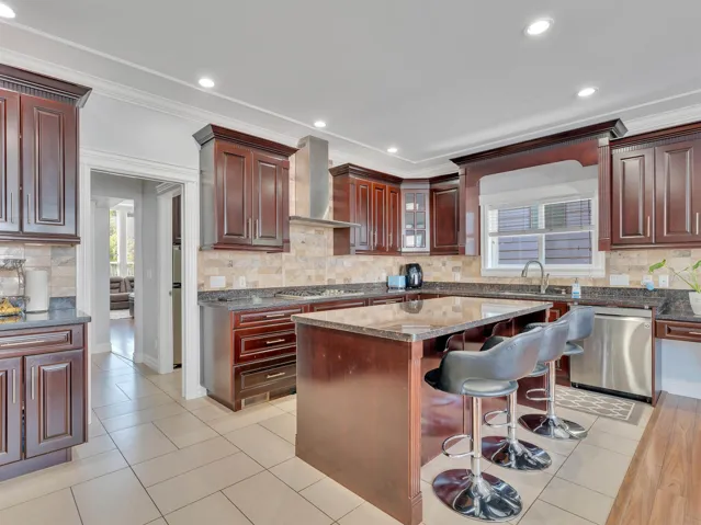 Kitchen featuring dark wood cabinetry, granite countertops, a tiled backsplash, and recessed lighting