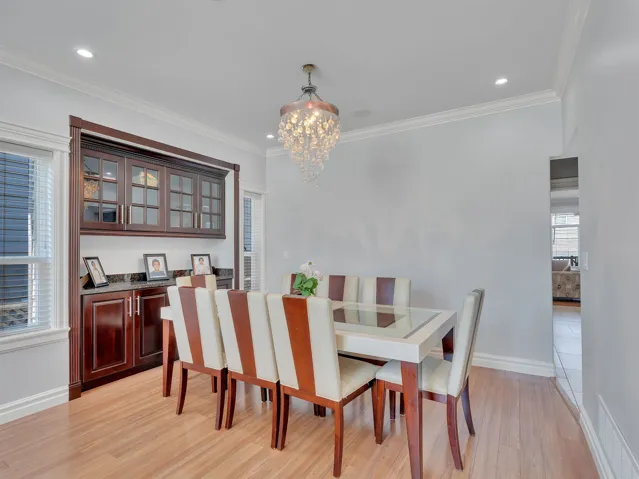 Dining area featuring wood-finish flooring, a built-in dark wood cabinetry unit with glass doors and a dark countertop, crown molding, recessed lighting, and a crystal chandelier