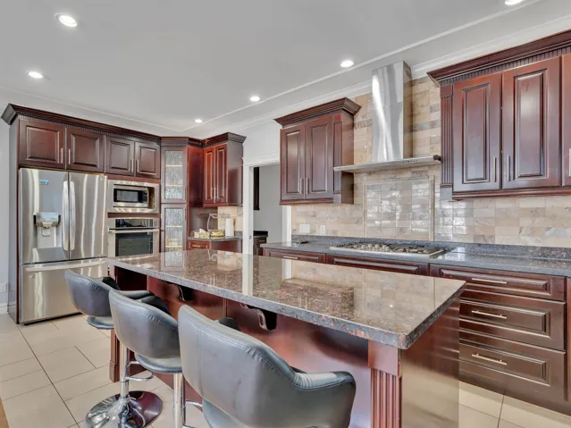 Spacious kitchen featuring dark wood-finish cabinetry, a large center island with a stone countertop, stainless steel appliances, a tile backsplash, and recessed lighting