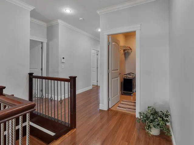 Hallway featuring wood-finish flooring, crown molding, recessed lighting, and a dark wood staircase with wrought iron balusters