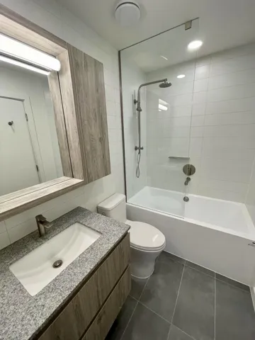 Bathroom with vanity, dark tile patterned flooring, washtub / shower combination, and tile walls