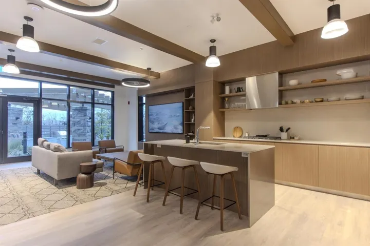 Kitchen with modern cabinets, hanging light fixtures, a center island with sink, and beamed ceiling