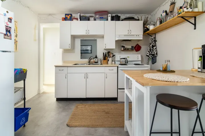 Kitchen with white appliances, white cabinetry, under cabinet range hood, a sink, and a breakfast bar area