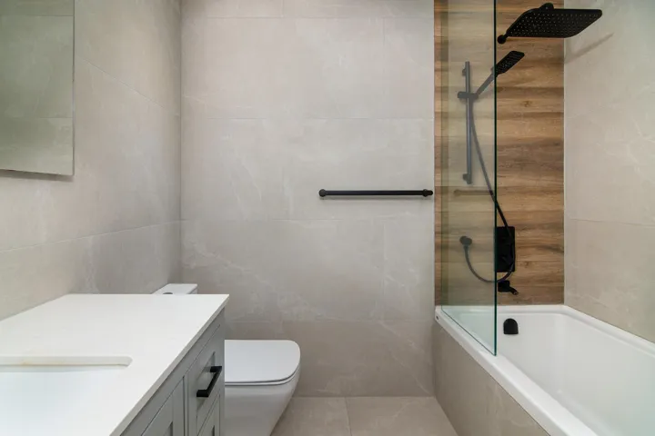 Full bathroom featuring toilet, tiled shower / bath, vanity, and tile walls
