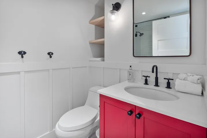 Full bath featuring wainscoting, a decorative wall, vanity, toilet, and a shower
