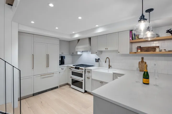 Kitchen with custom exhaust hood, light countertops, a sink, light wood-style flooring, and premium appliances