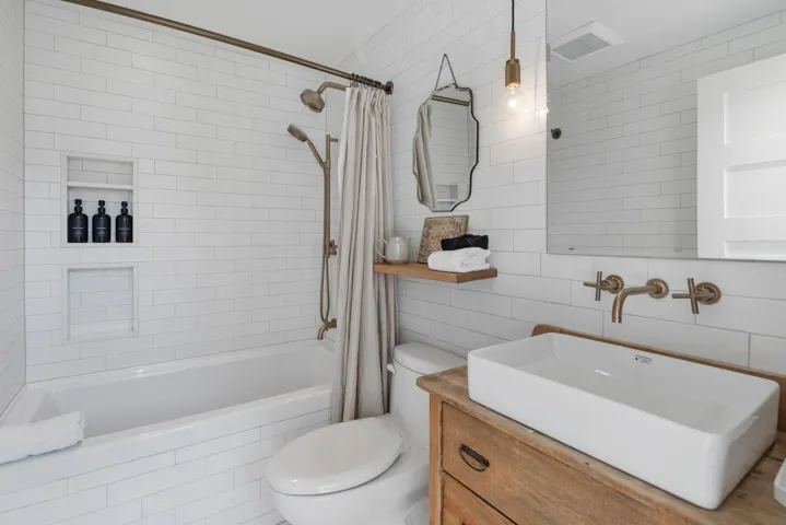 Bathroom with vanity, toilet, shower / bath combination with curtain, tile walls, and visible vents