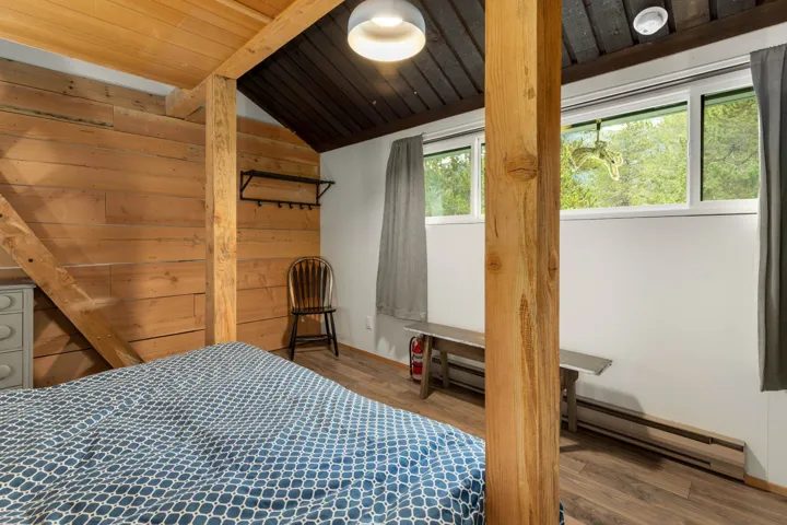 Bedroom featuring vaulted ceiling, a baseboard heating unit, wooden walls, and wood finished floors