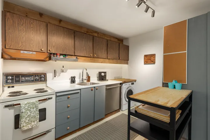 Kitchen featuring white electric range, light countertops, washer / clothes dryer, under cabinet range hood, and dishwasher