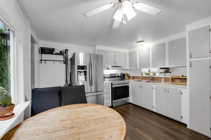 Kitchen featuring appliances with stainless steel finishes, dark wood-style floors, light countertops, white cabinetry, and ceiling fan