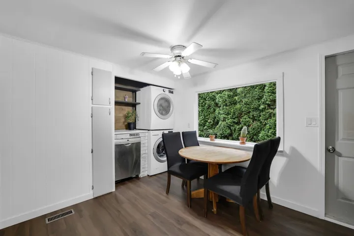 Dining area with dark wood-type flooring, stacked washing machine and dryer, and a ceiling fan