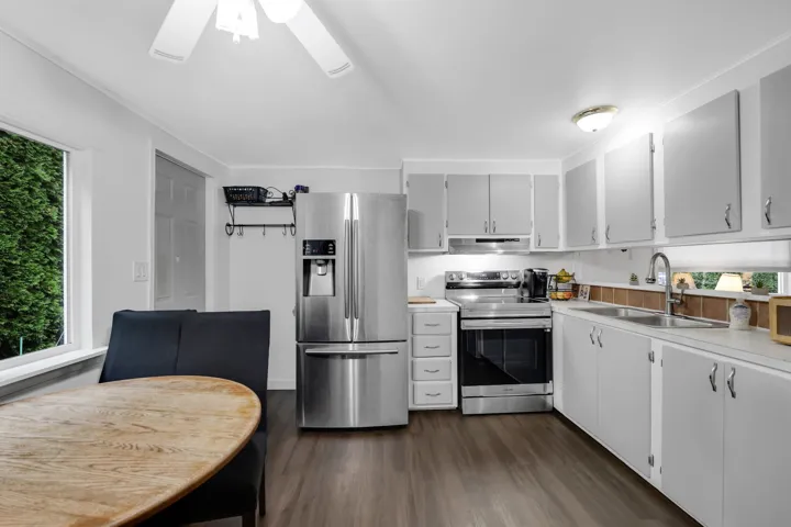 Kitchen with appliances with stainless steel finishes, light countertops, dark wood-type flooring, white cabinetry, and under cabinet range hood