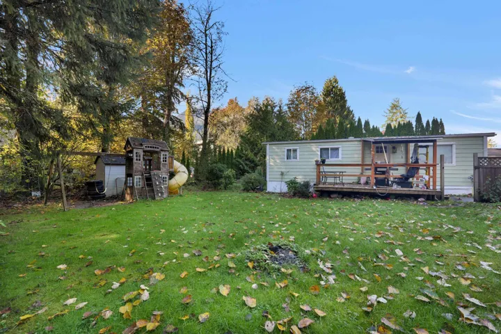 Back of house featuring a lawn, a wooden deck, and view of wooded area