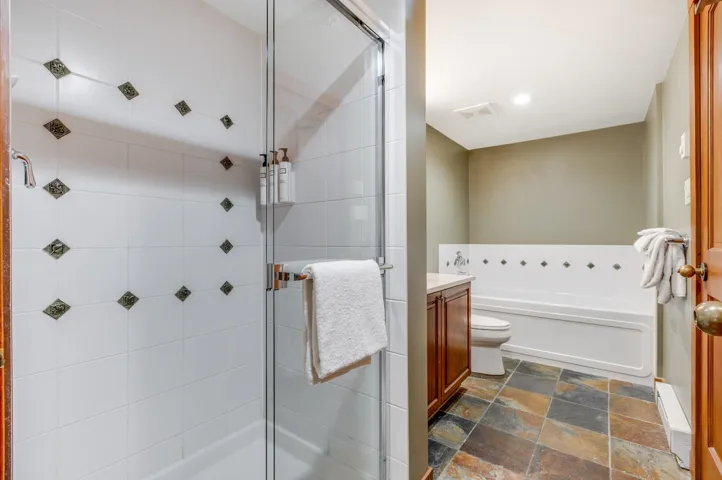 Bathroom featuring vanity, a stall shower, dark stone finish floors, a garden tub, and recessed lighting
