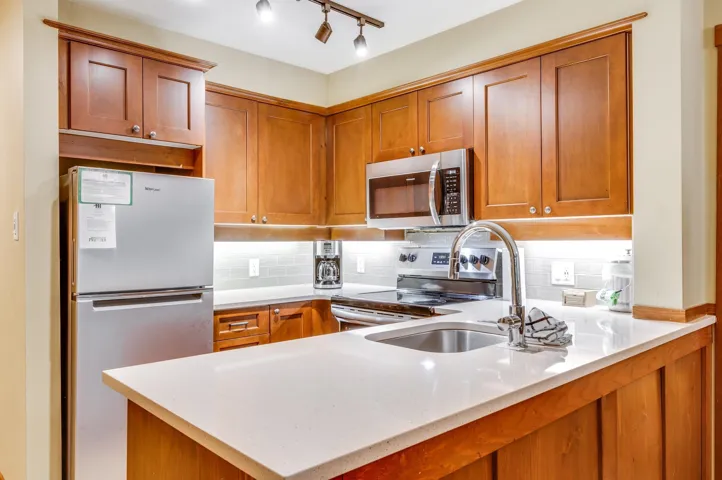 Kitchen featuring stainless steel appliances, tasteful backsplash, brown cabinetry, light stone countertops, and a peninsula