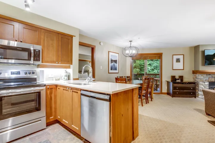 Kitchen with stainless steel appliances, a peninsula, decorative light fixtures, light carpet, and brown cabinets