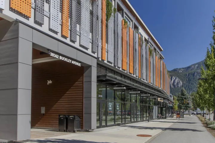 Modern commercial building with a mountain backdrop, featuring a street-level pedestrian entrance and ground-floor retail spaces