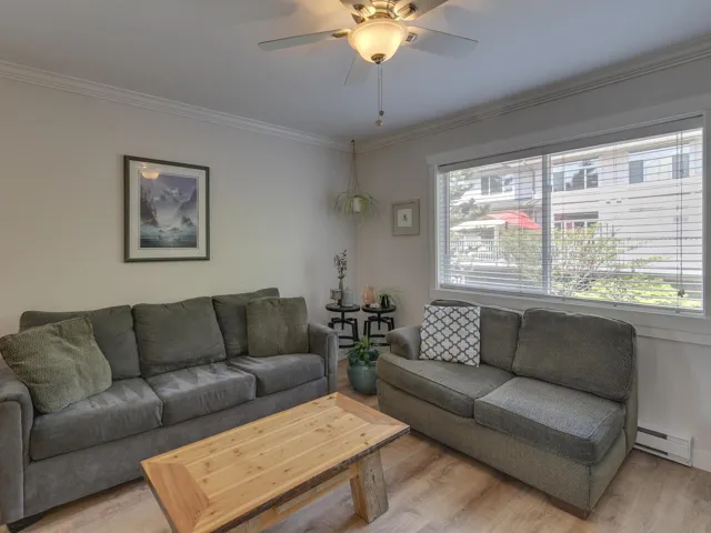 Living room featuring light wood-type flooring, crown molding, baseboard heating, and a ceiling fan