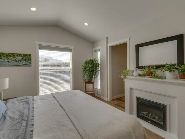 Bedroom with light wood finished floors, vaulted ceiling, a glass covered fireplace, baseboards, and recessed lighting