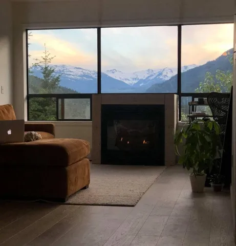 Living room with a warm lit fireplace, wood finished floors, and a mountain view