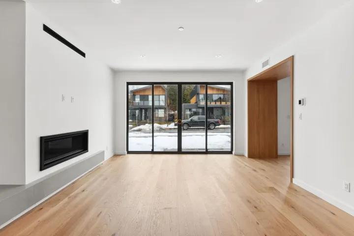 Unfurnished living room with wood finished floors, a glass covered fireplace, visible vents, and baseboards
