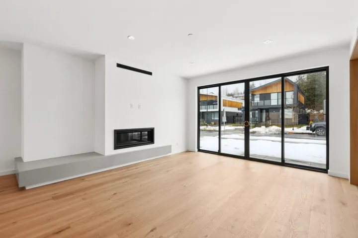 Unfurnished living room with a glass covered fireplace, wood finished floors, and baseboards