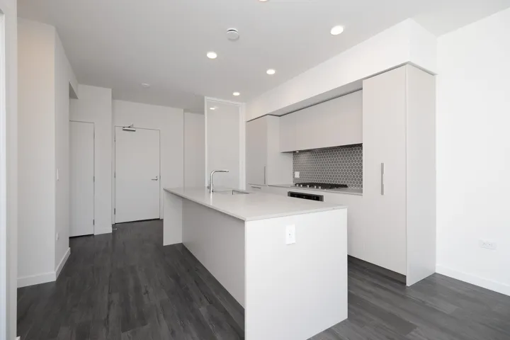 Kitchen featuring modern cabinets, white cabinetry, light countertops, dark wood-style floors, and a kitchen island with sink