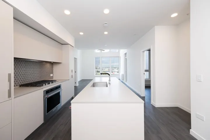 Kitchen featuring dark wood-style flooring, an island with sink, stainless steel appliances, backsplash, and light countertops