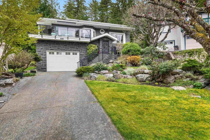 View of front of property featuring stone siding, driveway, a garage, and a front yard