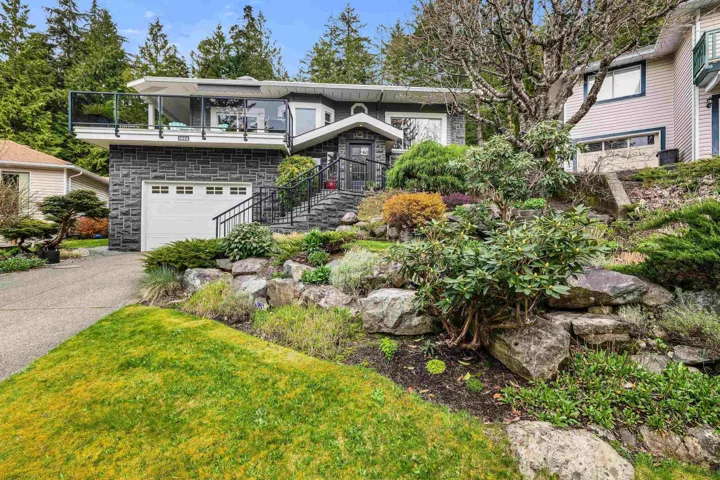 View of front of property featuring stone siding, a garage, driveway, and a balcony