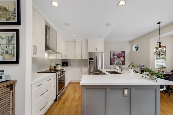 Kitchen featuring stainless steel appliances, a spacious island, backsplash, light wood-type flooring, and a chandelier