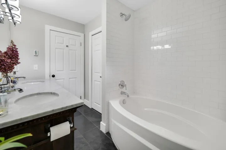 Full bath with double vanity, dark tile patterned flooring, and tub / shower combination