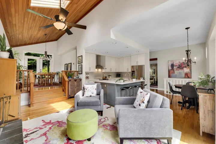 Living room with suspended lighting, a ceiling fan, light wood-type flooring, a vaulted wood ceiling, and a skylight