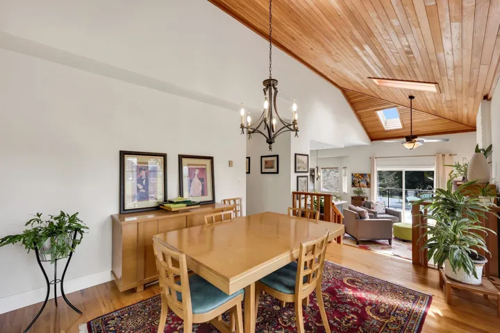 Dining space with a skylight, a vaulted wood ceiling, light wood finished floors, ceiling fan, and a chandelier