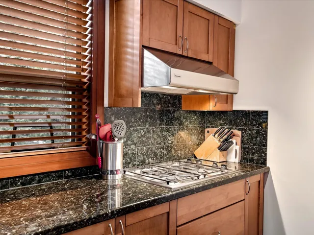 Kitchen featuring stainless steel appliances, tasteful backsplash, stone finish flooring, ventilation hood, and baseboards