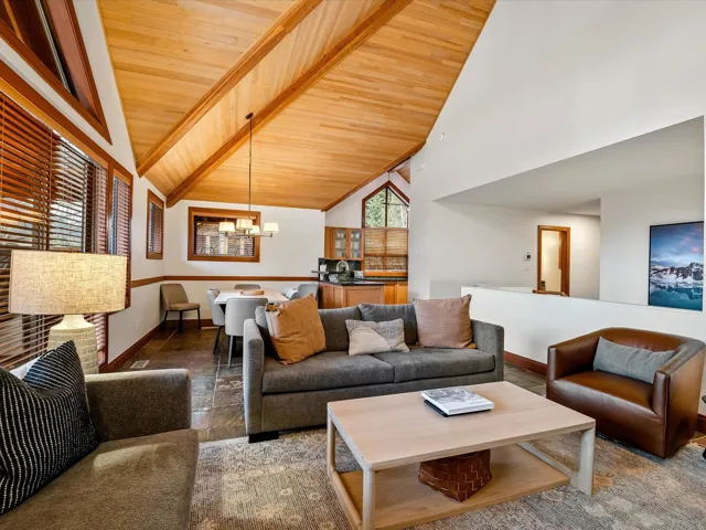 Living area with high vaulted ceiling, visible vents, a stone fireplace, and an inviting chandelier