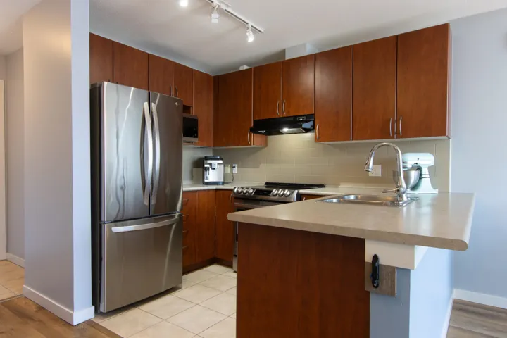 Kitchen with a peninsula, appliances with stainless steel finishes, tasteful backsplash, light countertops, and under cabinet range hood
