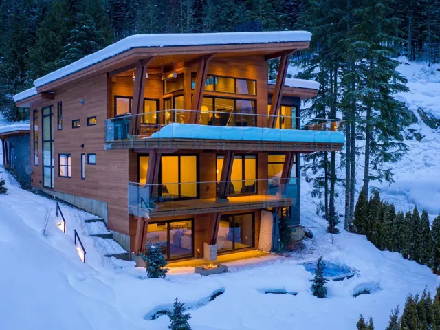 Snow covered back of property with a balcony and a forest view