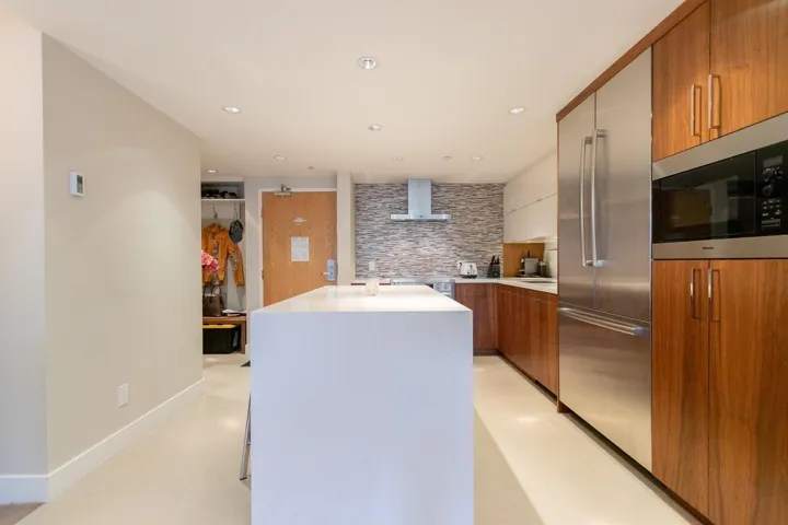 Kitchen with brown cabinetry, appliances with stainless steel finishes, modern cabinets, wall chimney exhaust hood, and a kitchen island