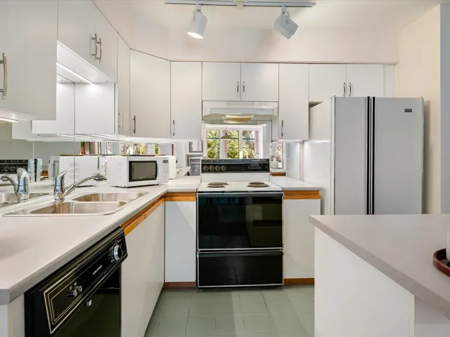 Kitchen with white cabinetry, light countertops, white appliances, under cabinet range hood, and a sink