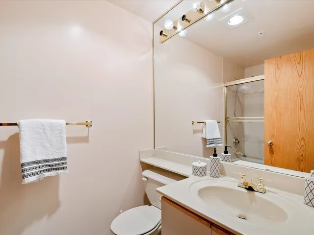 Full bath featuring a shower with door, toilet, and vanity