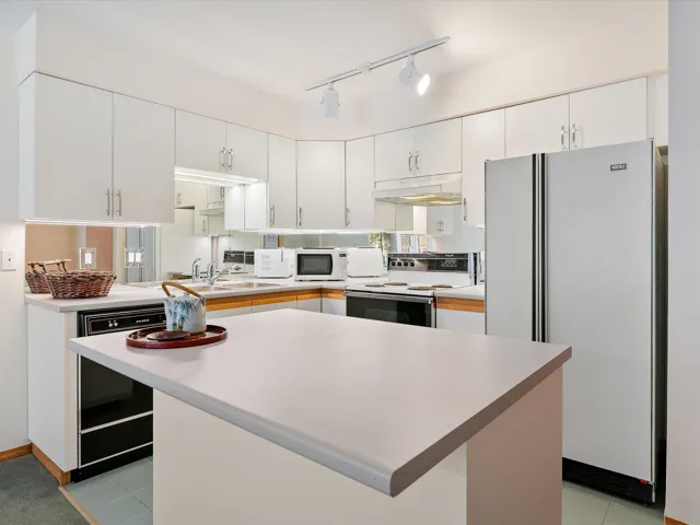 Kitchen featuring light countertops, under cabinet range hood, white appliances, white cabinets, and decorative backsplash