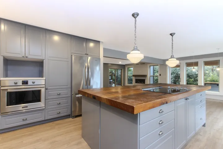 Kitchen with butcher block counters, stainless steel appliances, hanging light fixtures, gray cabinets, and light wood-style floors