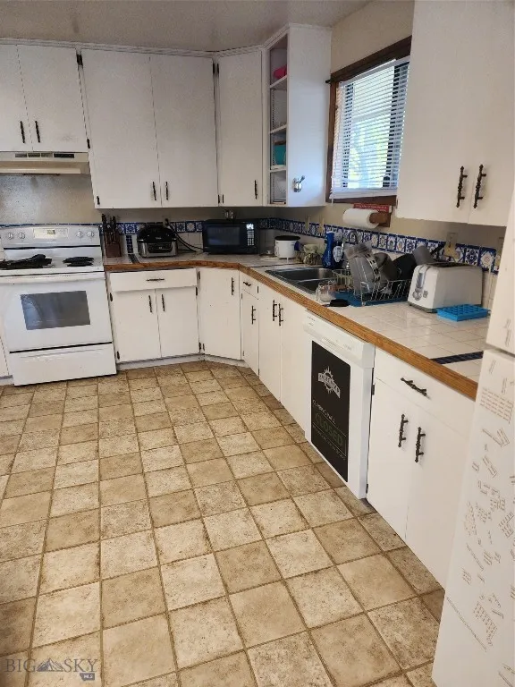 Kitchen with range hood, white cabinetry, range, dishwashing machine, and tile countertops