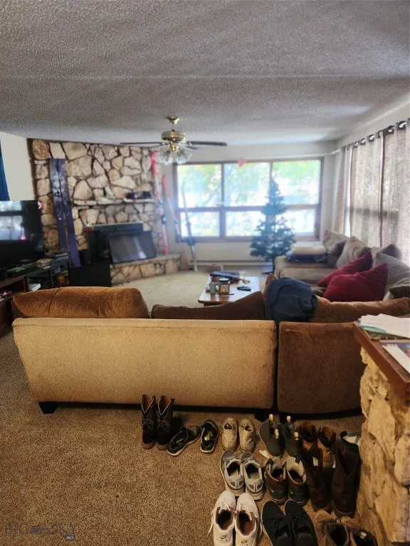Living room featuring a textured ceiling, carpet flooring, ceiling fan, and a fireplace
