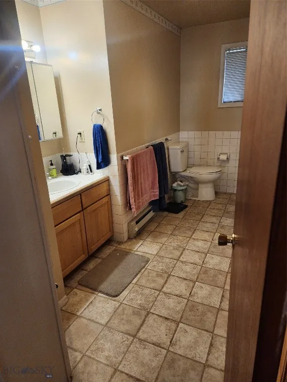 Bathroom featuring tile walls, a baseboard heating unit, vanity, and toilet