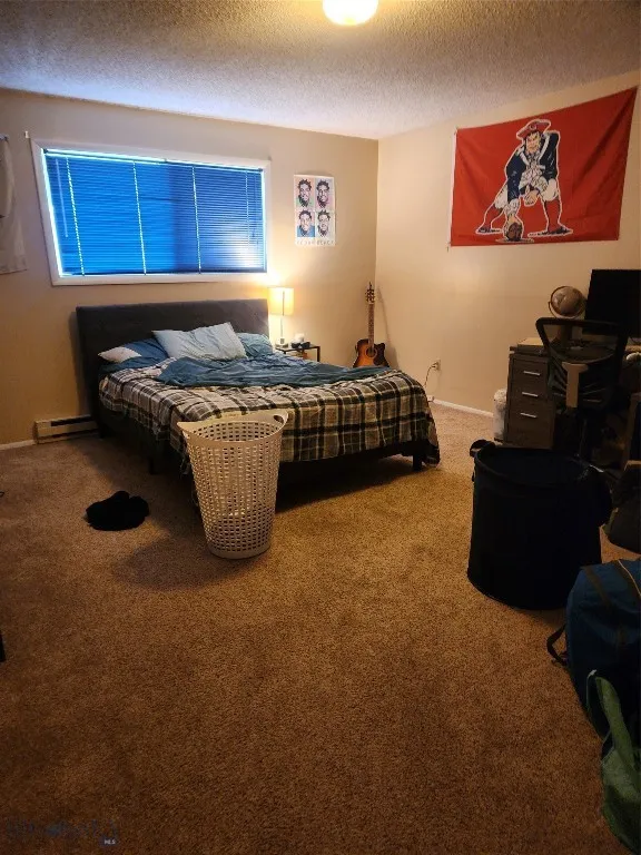 Carpeted bedroom with baseboard heating and a textured ceiling
