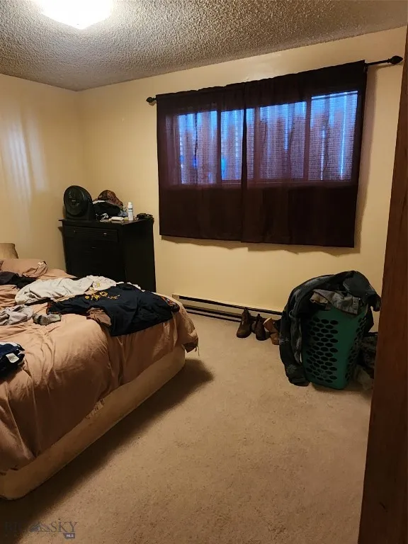 Bedroom featuring a baseboard heating unit, carpet, and a textured ceiling
